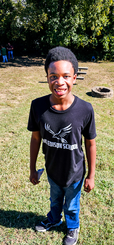 A student in an Edison School T-shirt smiling outside on the school lawn
