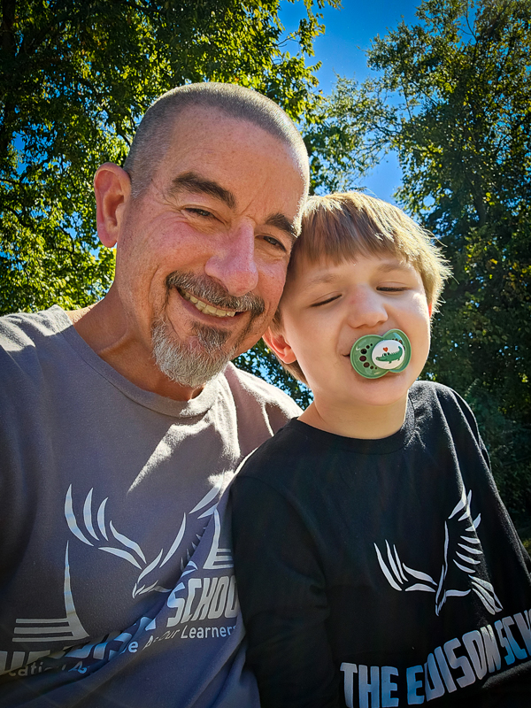 A staff member and a young student, both in Edison School shirts, outdoors on a sunny day