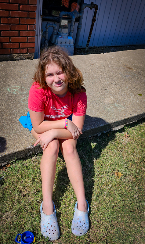 A student sitting on a step outside, smiling in the sun
