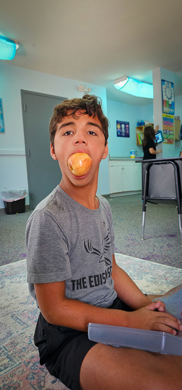 A student grinning with a doughnut in his mouth during a classroom celebration