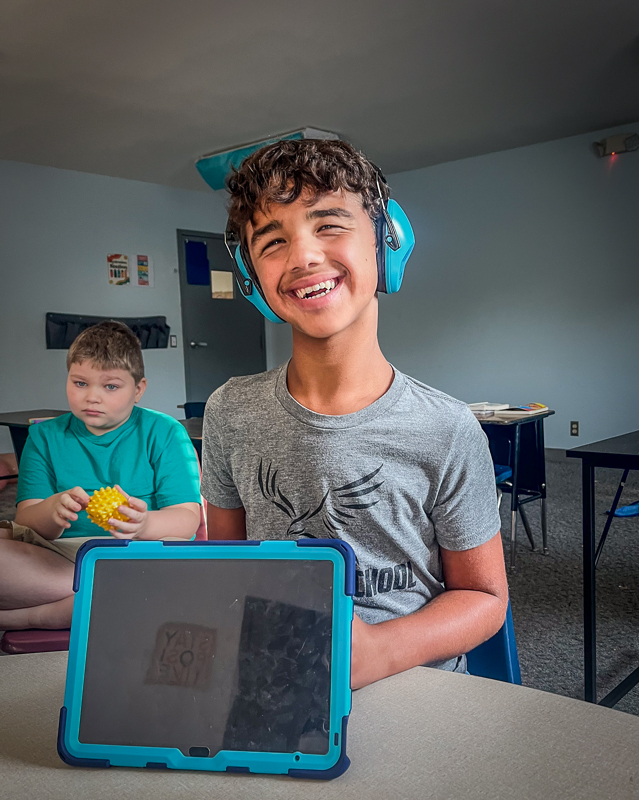 A student in ear defenders working at his tablet in class