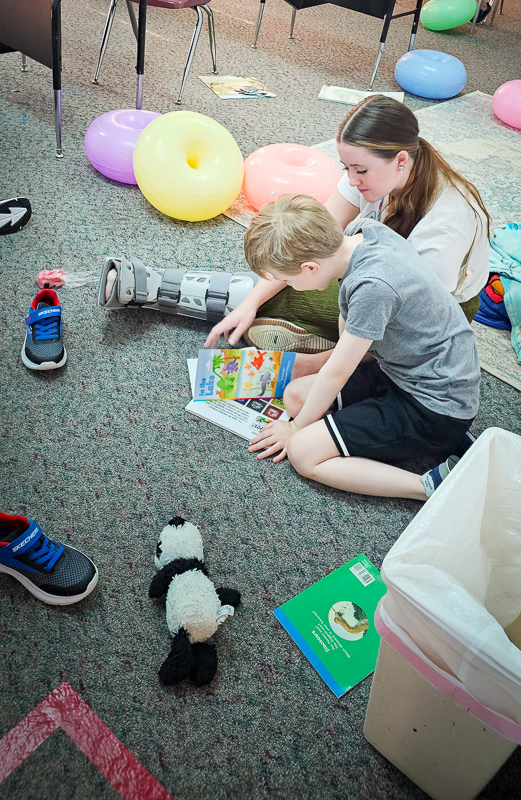 A teacher sitting on the classroom floor, working with a student