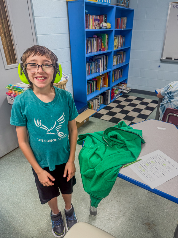 A student in ear defenders and an Edison School T-shirt smiling in the classroom library