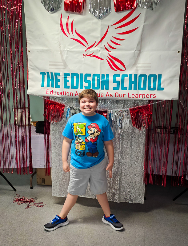 A student standing in front of The Edison School banner at a school event