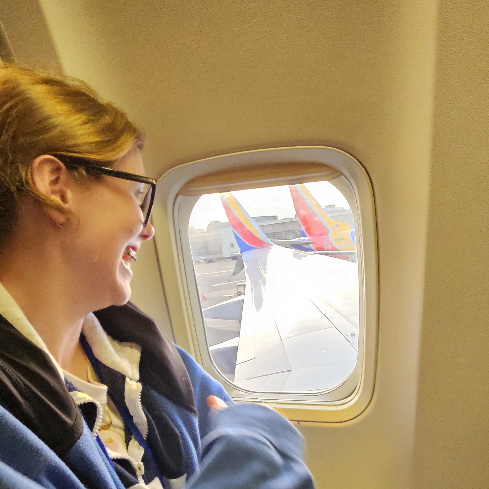 Austin smiling as she looks out of an airplane window on her first ever flight
