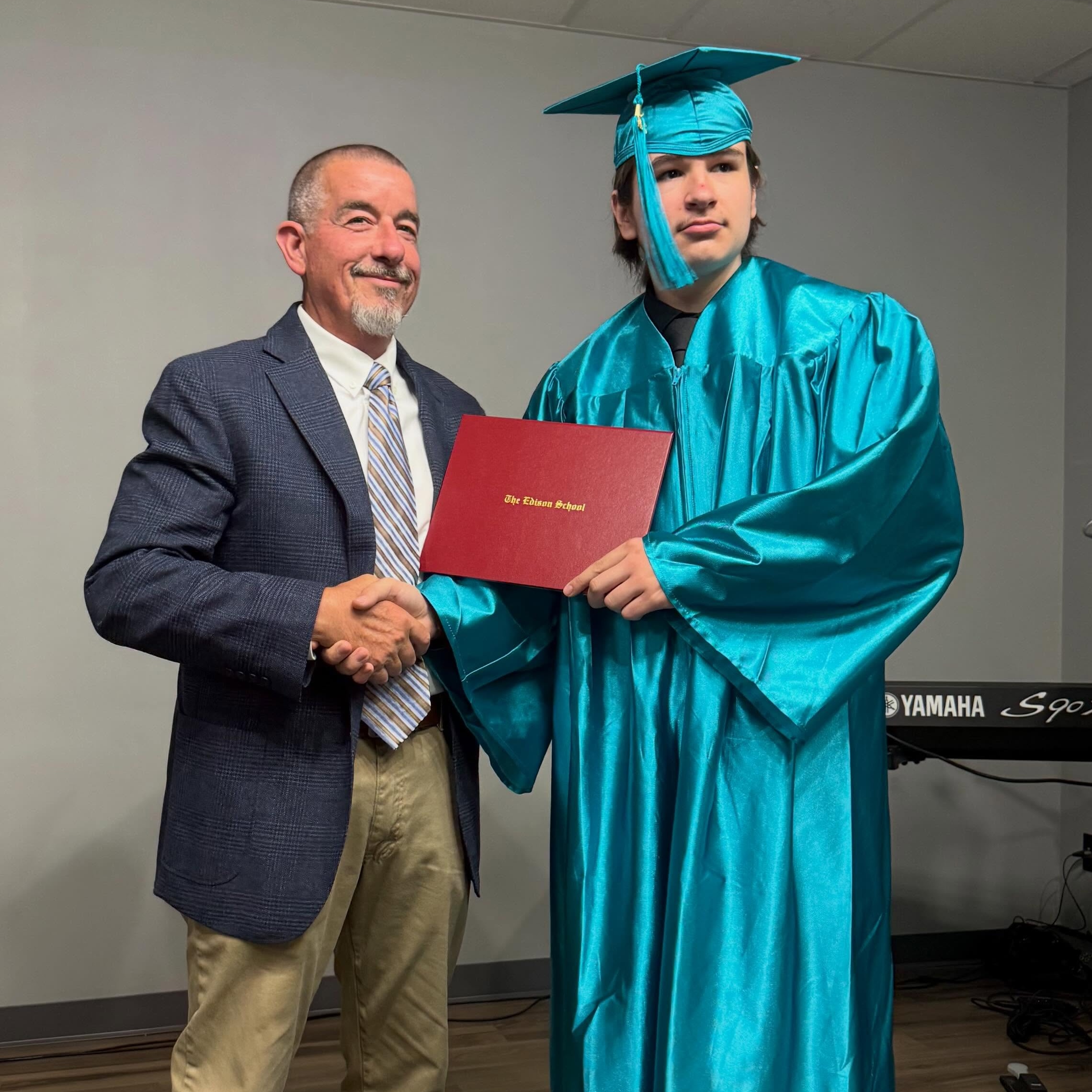 Gabe in cap and gown shaking hands with Jon, Head of School, and holding his Edison School diploma