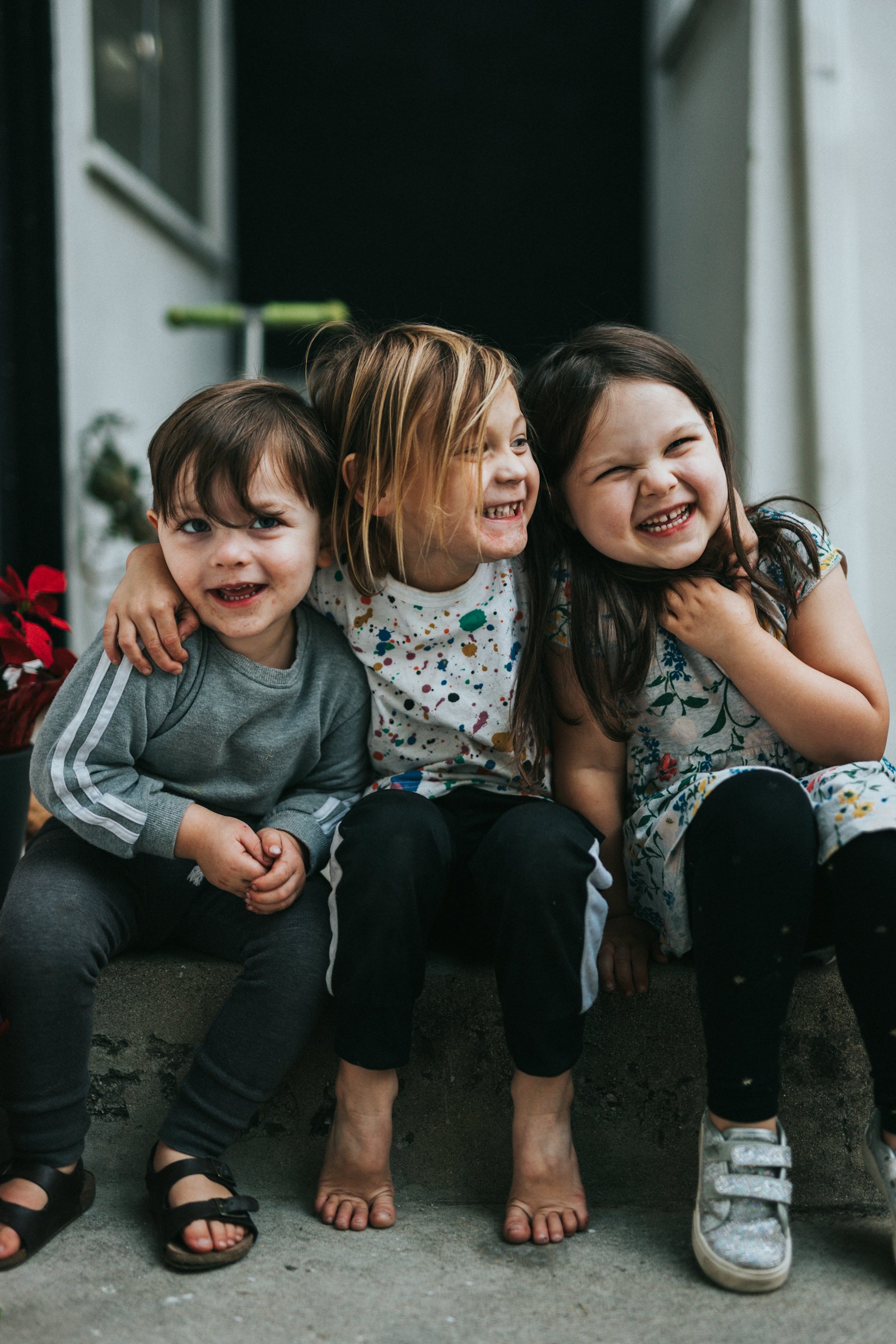 Three young children sitting together on a step, laughing