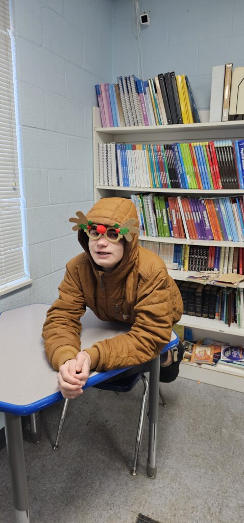 A student in a reindeer headband smiling at his desk in the classroom