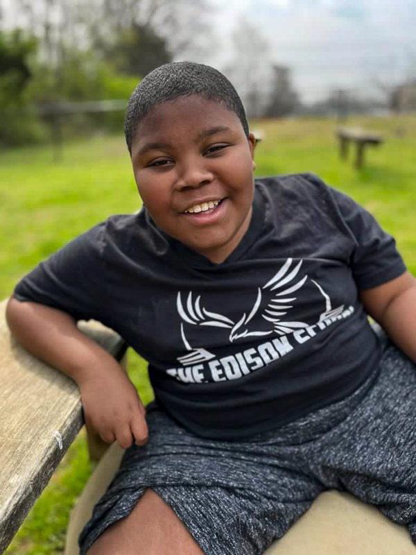 A smiling student in an Edison School T-shirt sitting on a bench outside
