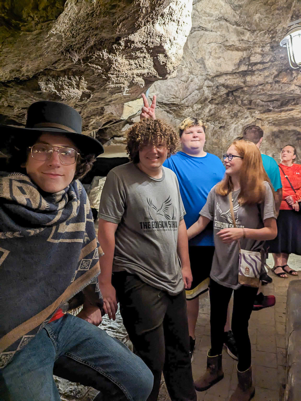 Edison students smiling for the camera inside a cave on a field trip, one in a cowboy hat and poncho