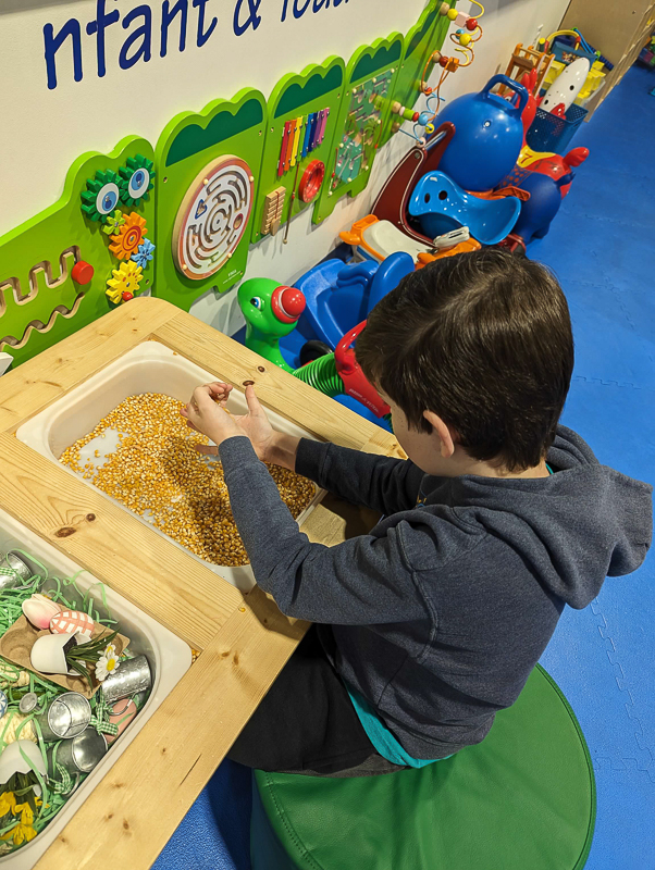 A student scooping dried corn in a sensory bin