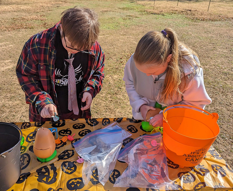 Two students building Mr. Potato Head toys at an outdoor table with a Halloween tablecloth