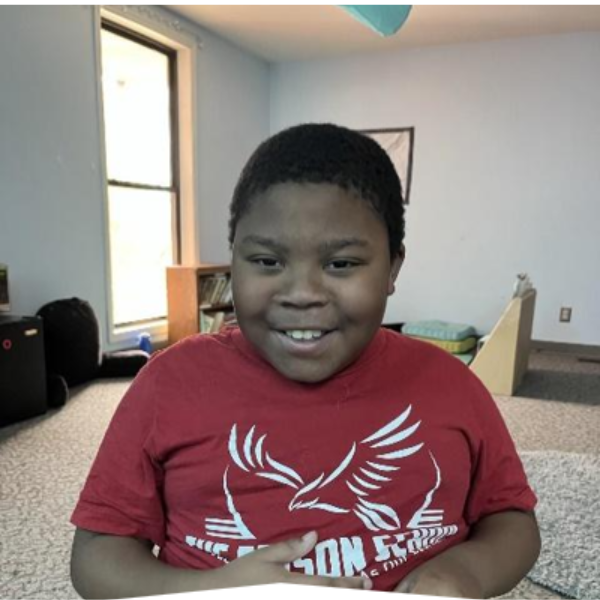 An Edison student in a red Edison School T-shirt, smiling in a classroom