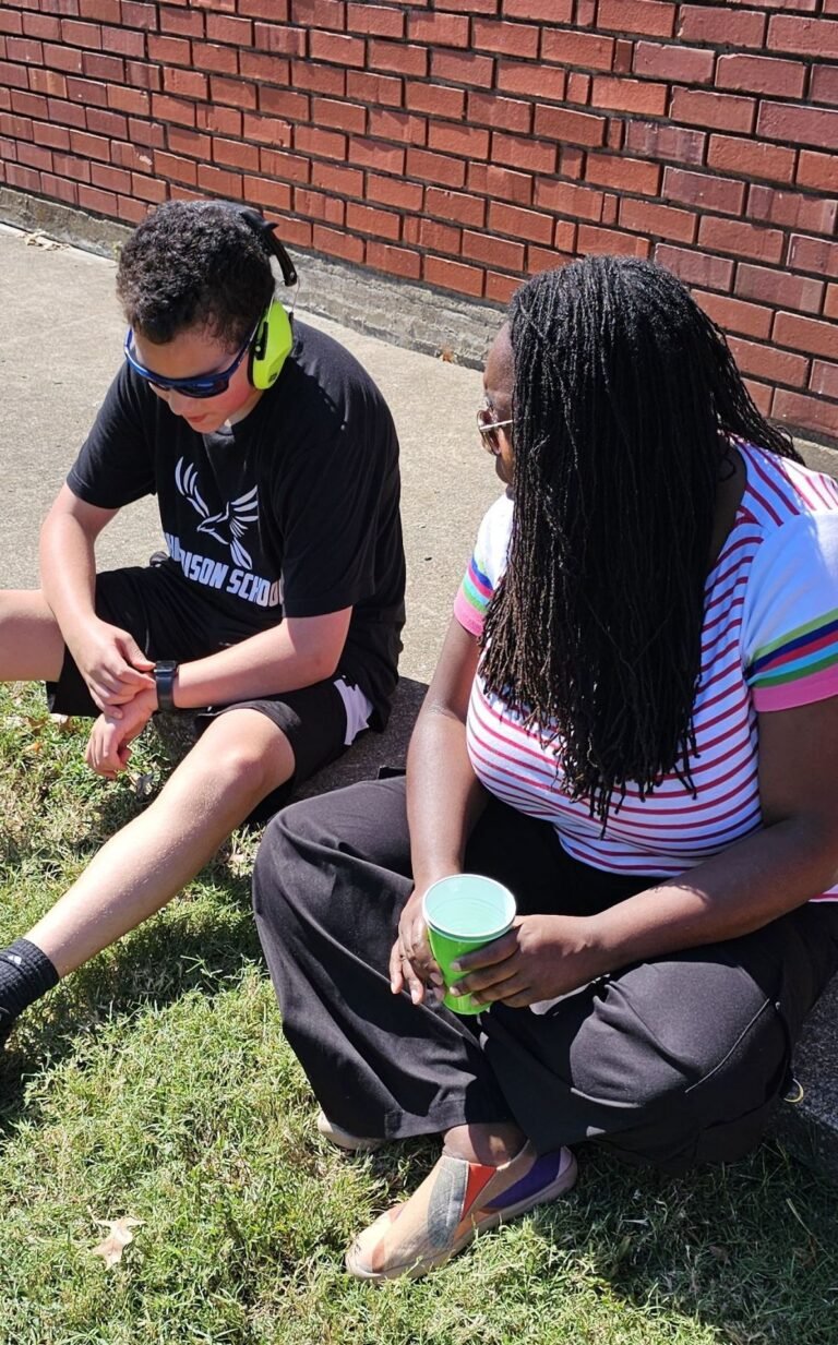 Two Edison students sitting on the grass against the school's brick wall, talking